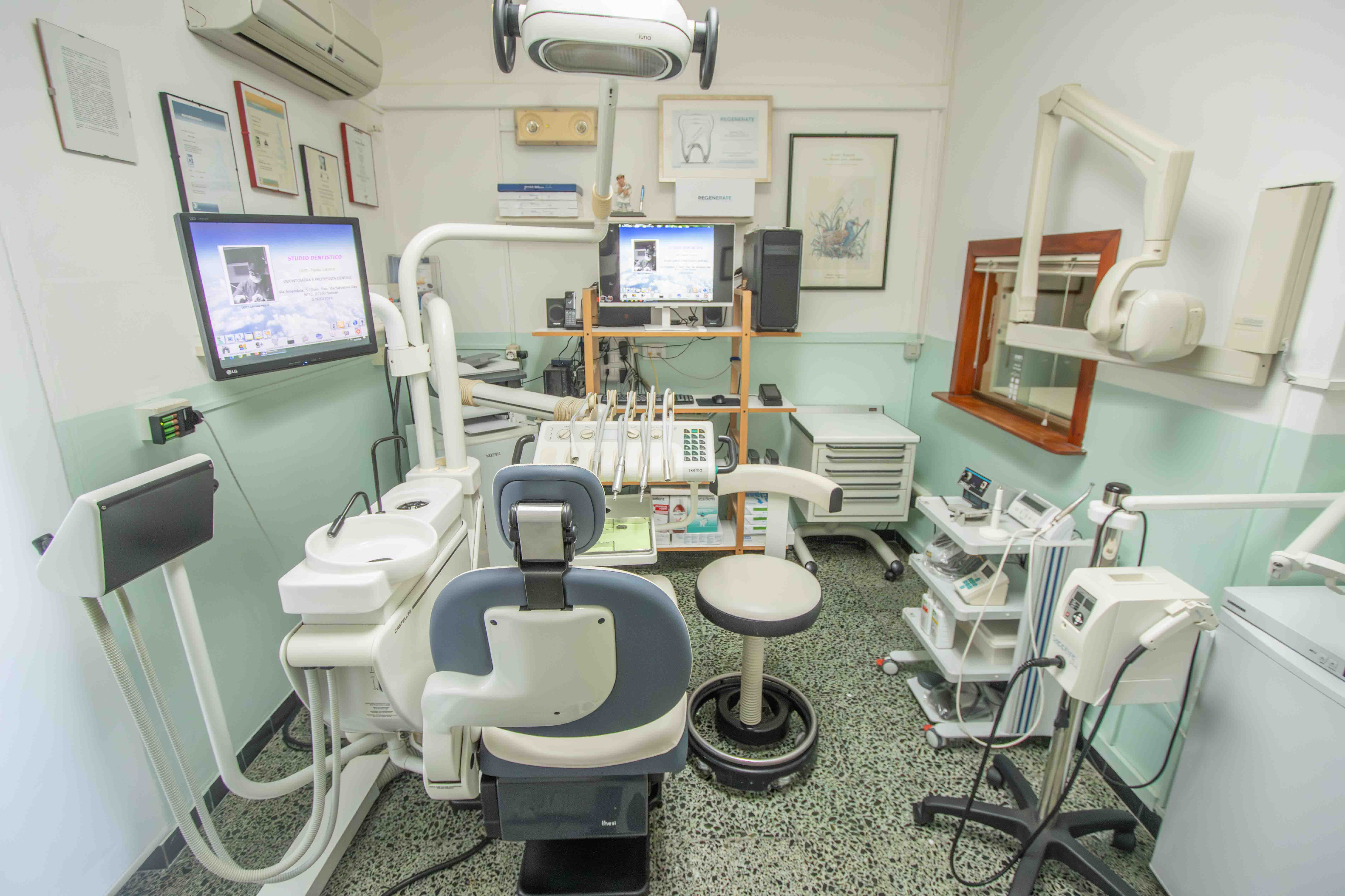 Stanza bianca dello studio con riunito odontoiatrico e monitor clinici